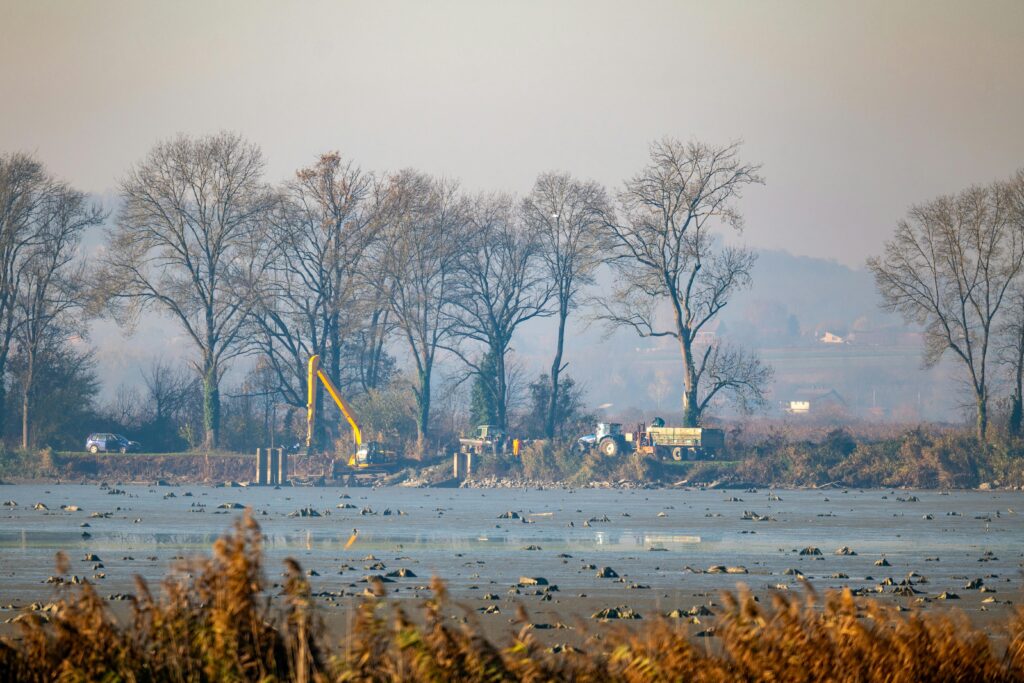 A serene landscape featuring a construction site with machinery, surrounded by bare trees in Garešnica, Croatia.